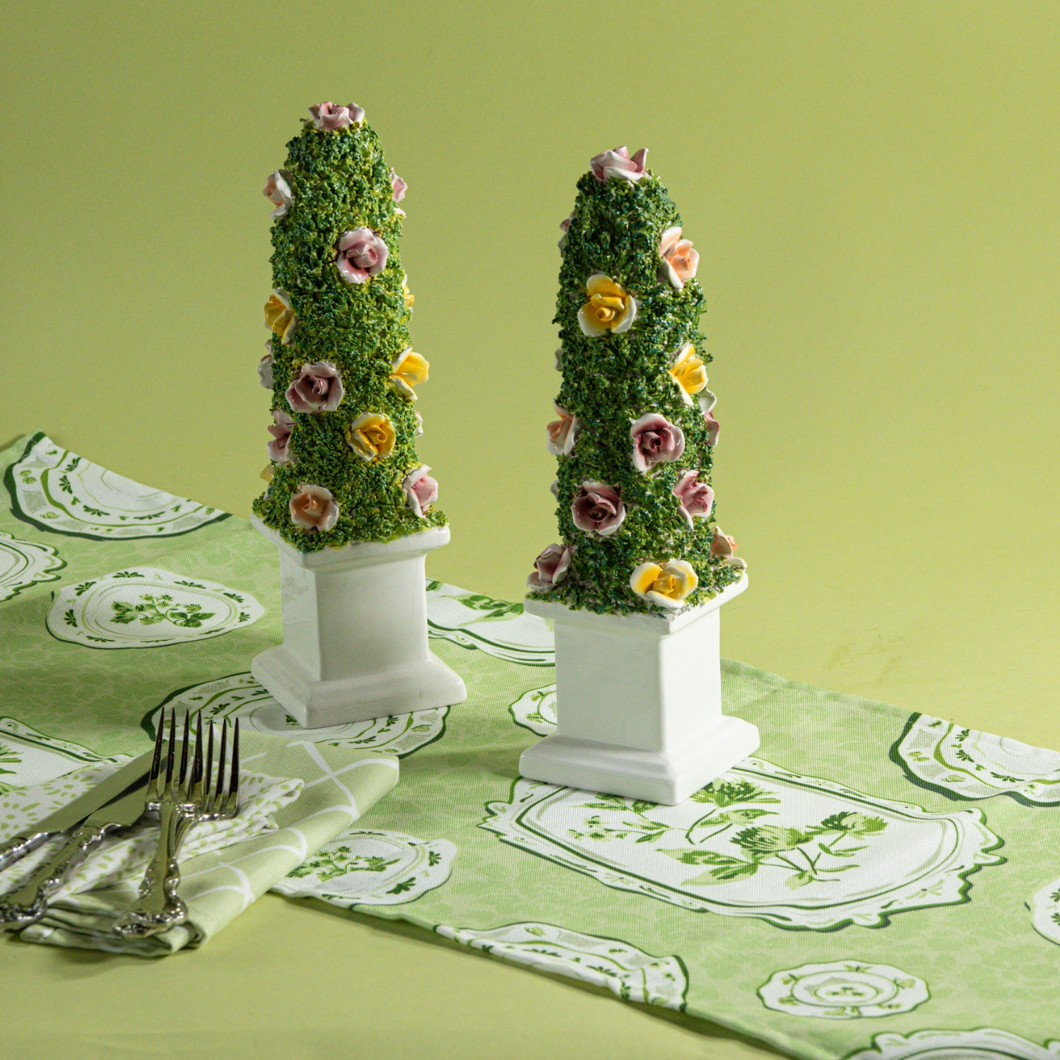 A pair of vintage ceramic topiaries studded with pink and yellow roses and resting on a green and white table runner from madcap cottage