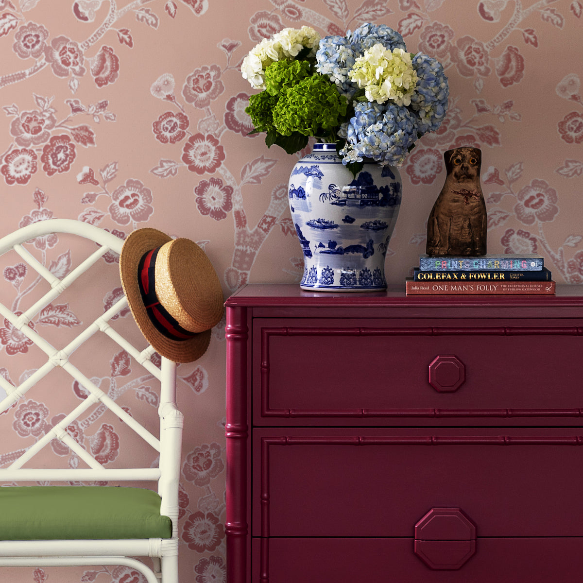 A large red chest and chinoiserie vase agains a wall of pink chinoiserie wallpaper