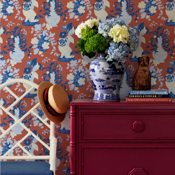 A red chest of drawers and chair against a wall of chinoiserie wallpaper with pug motifs.