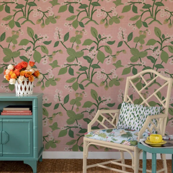 a room with a white chair and blue chest against a wall featuring pink lemon and strawberry wallpaper