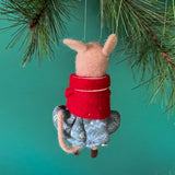 back of a felt mouse ornament wearing a red jacket and gray skirt holds a small brown teddy bear, hanging from a pine branch against a teal background.