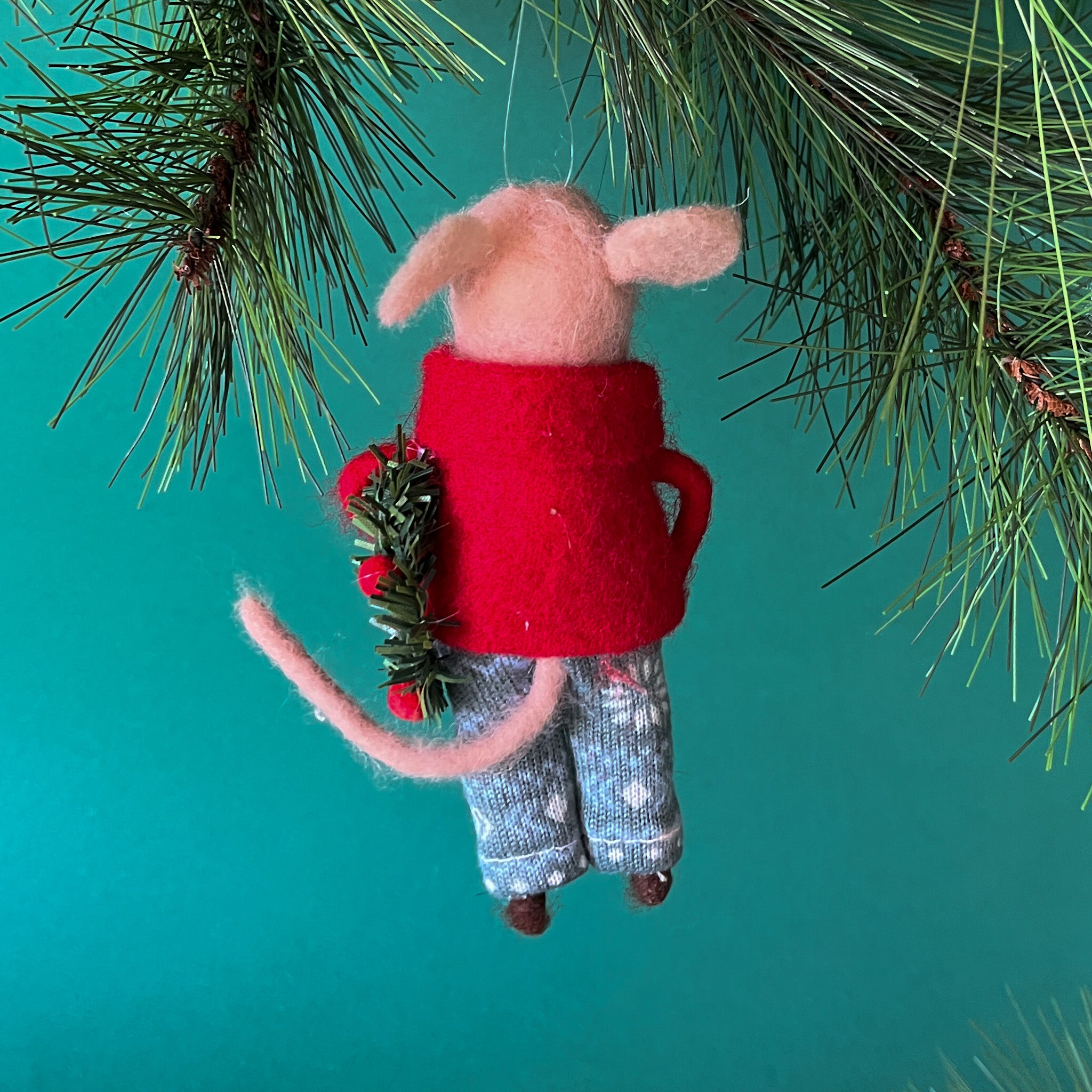 back of a felt mouse ornament wearing a red jacket and patterned blue-green pants, holding a festive green wreath with red accents.