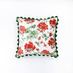 Square decorative pillow featuring a red and green floral geranium pattern on a white background, finished with a dark green scalloped trim around the edges.