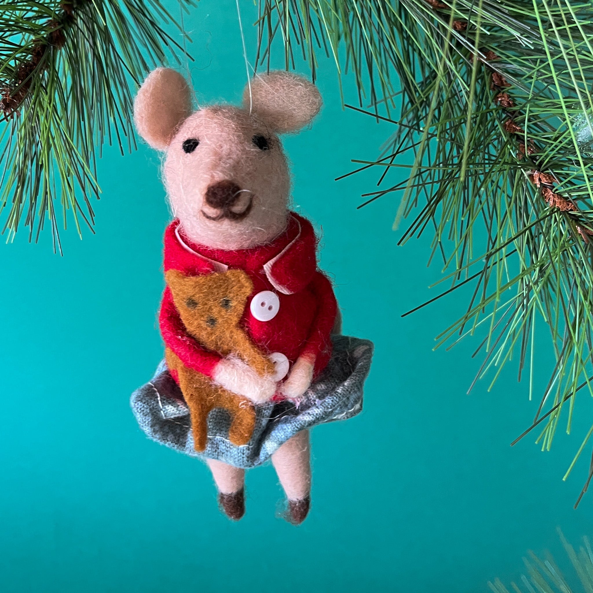 felt mouse ornament wearing a red jacket and gray skirt holds a small brown teddy bear, hanging from a pine branch against a teal background.