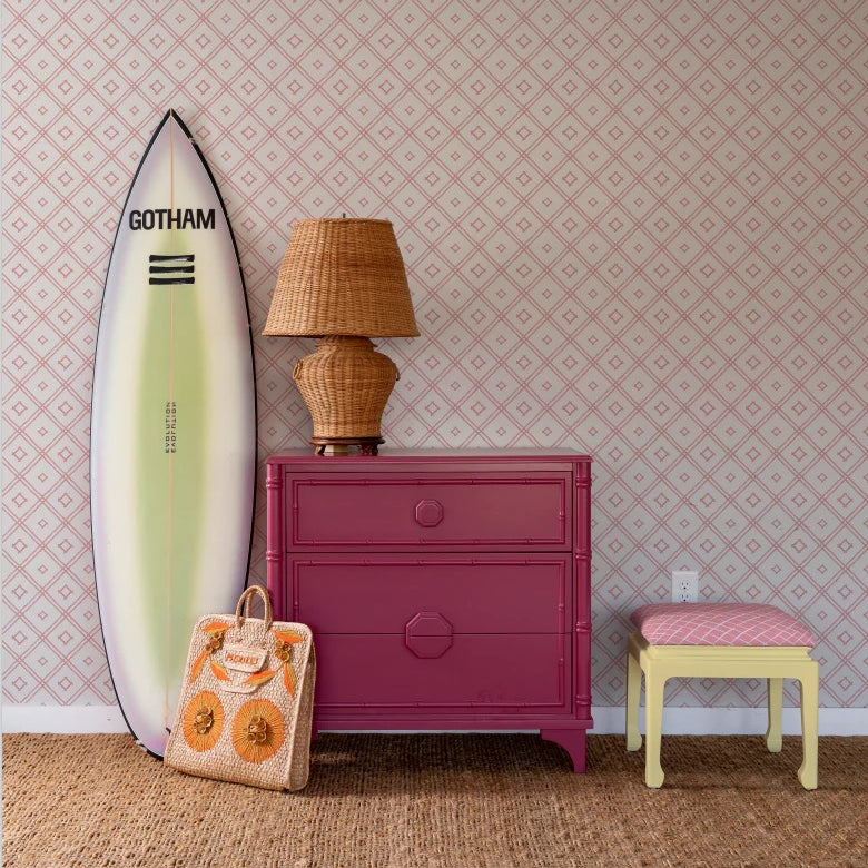 a surfboard and red chest in front of a pink bamboo trellis wallpaper design on a white background from Madcap Cottage