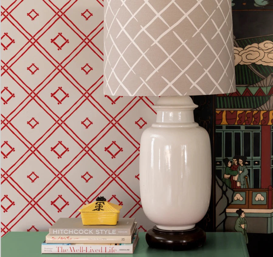 beige lamp agains a wall of red and white wallpaper in a bamboo trellis design.