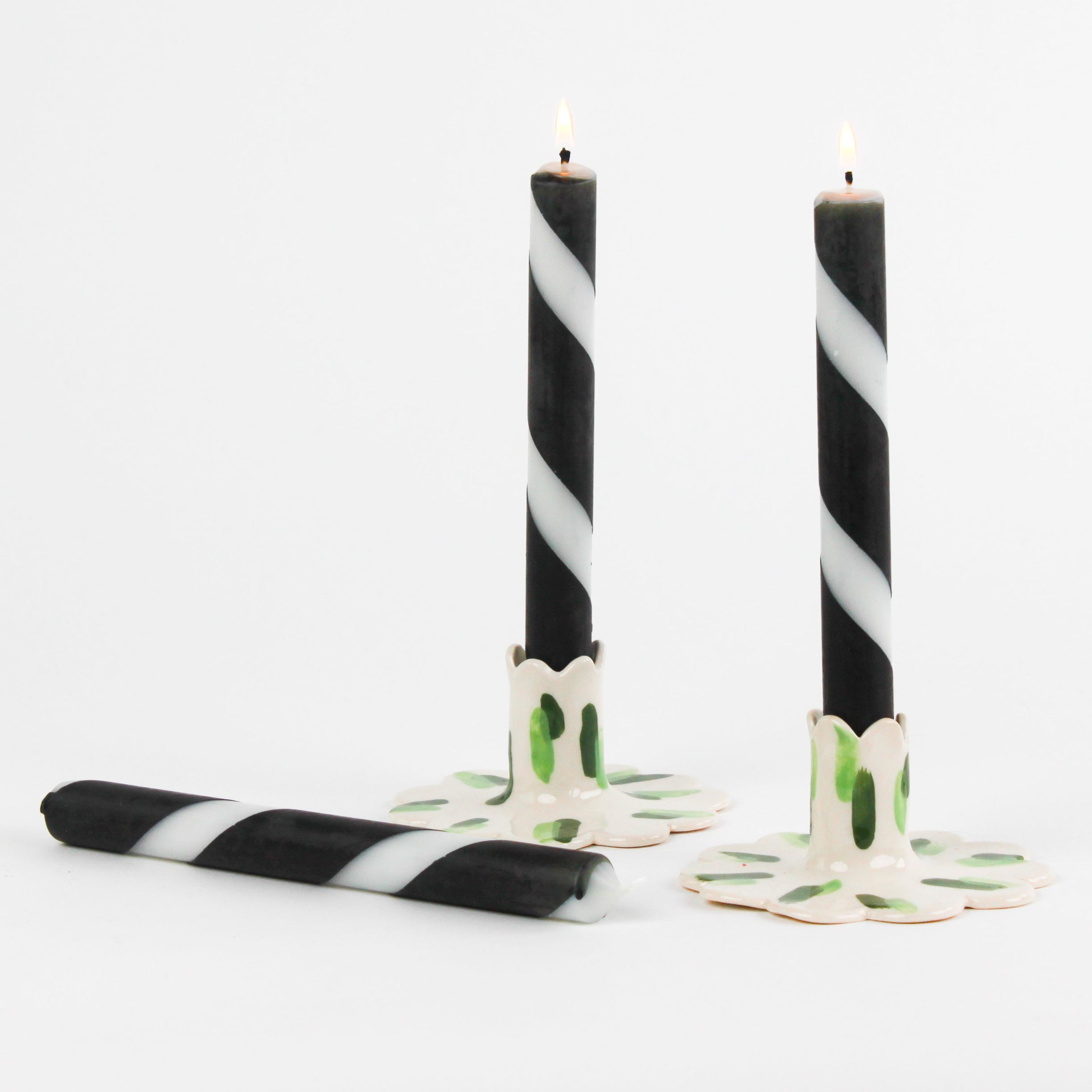 lit 2 white and black striped Taper Candles candle holders and 1 lying horizontally in a white background