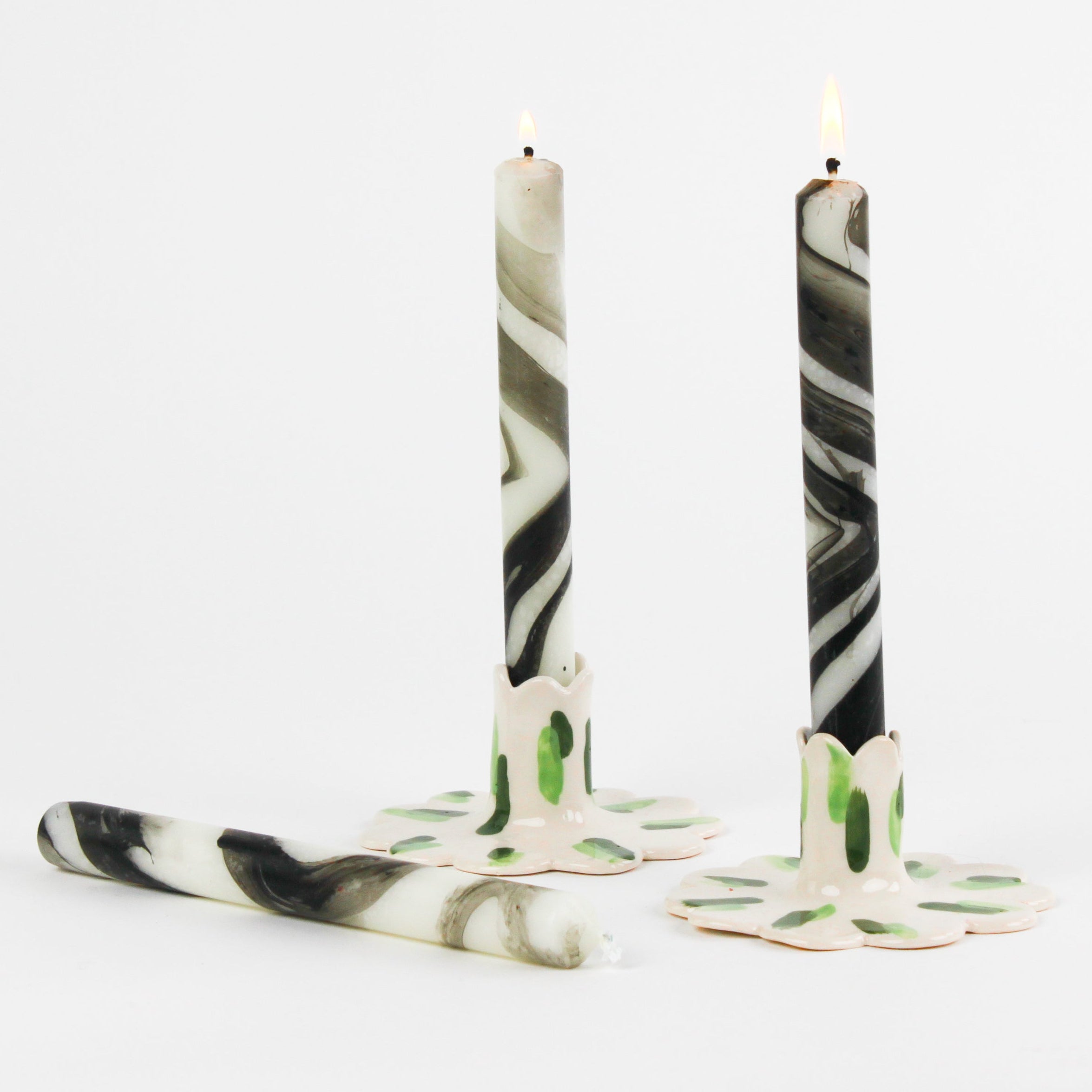 lit 2 marbled white and black Taper Candles candle holders and 1 lying horizontally in a white background