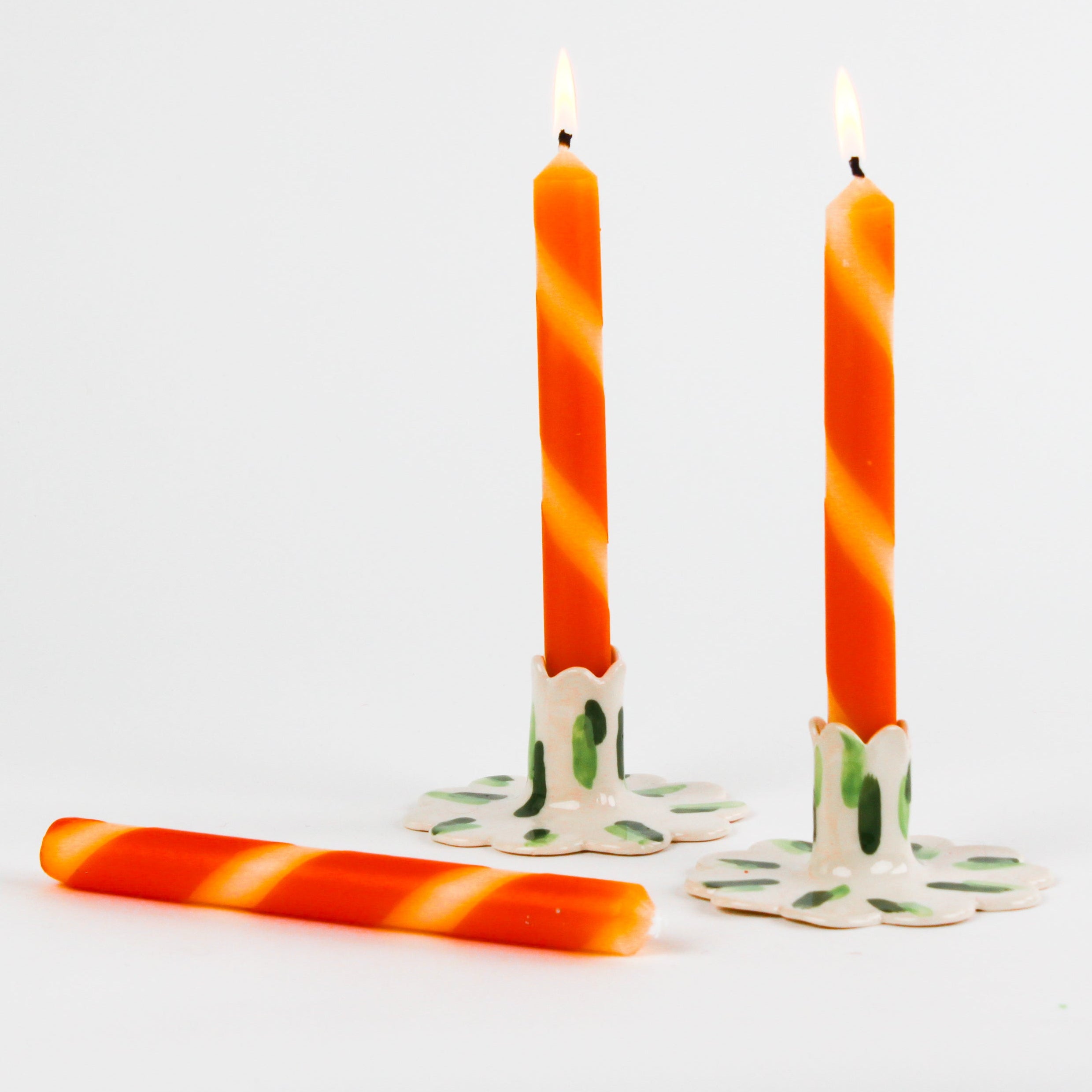 lit Three orange and white stripe taper candles in white background