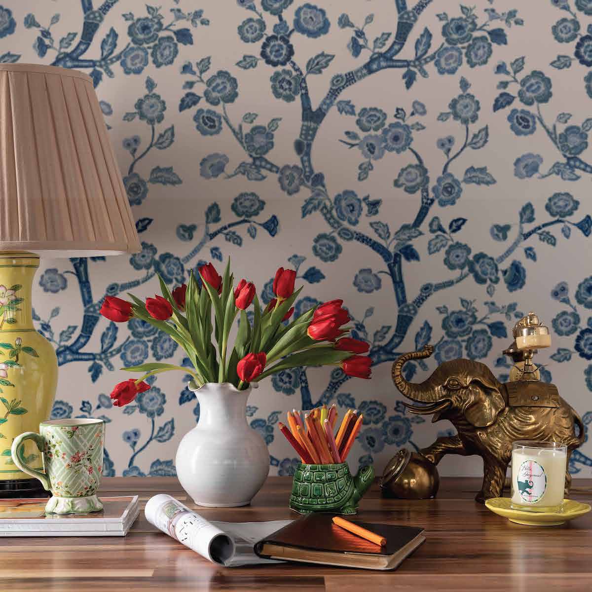 A desk featuring a tulip filled vase against blue and white chinoiserie wallpaper