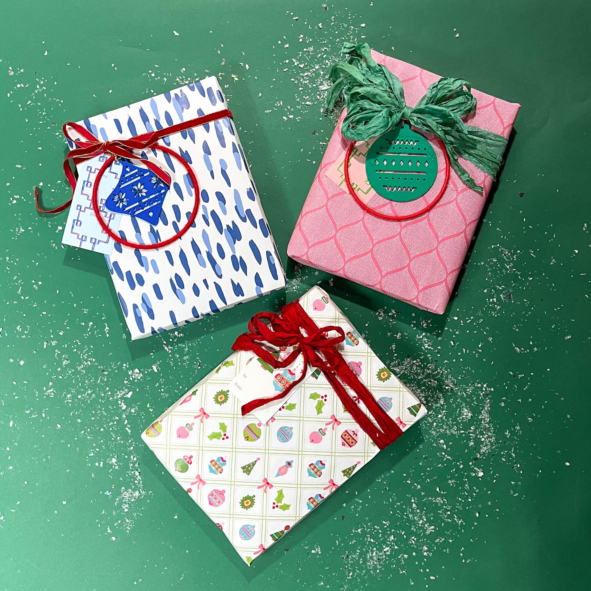 Three christmas gifts wrapped in colorful christmas wrapping paper from Madcap Cottage on a green background.