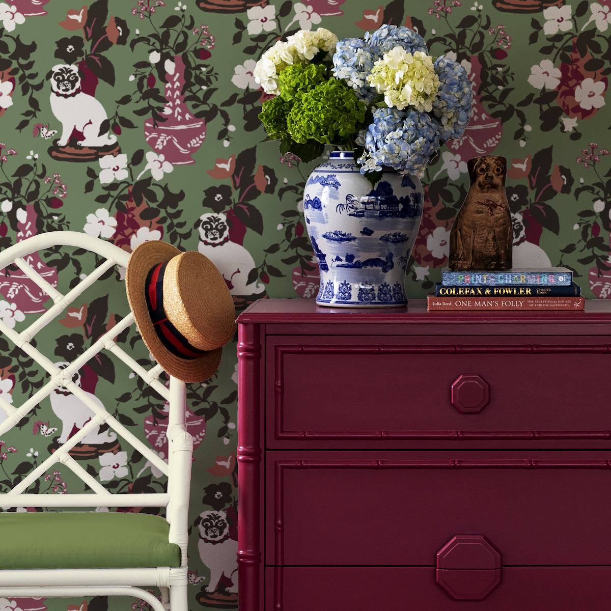Red drawers and vase against a wall of green chinoiserie wallpaper with a pug motif.