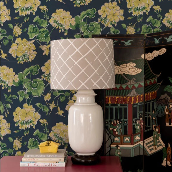 Room featruing a beige lamp on a table with navy and yellow geranium wallpaper in the background.