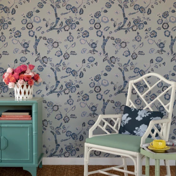 a white chair and blue sidetable against a wall of light blue and white chinoiserie wallpaper