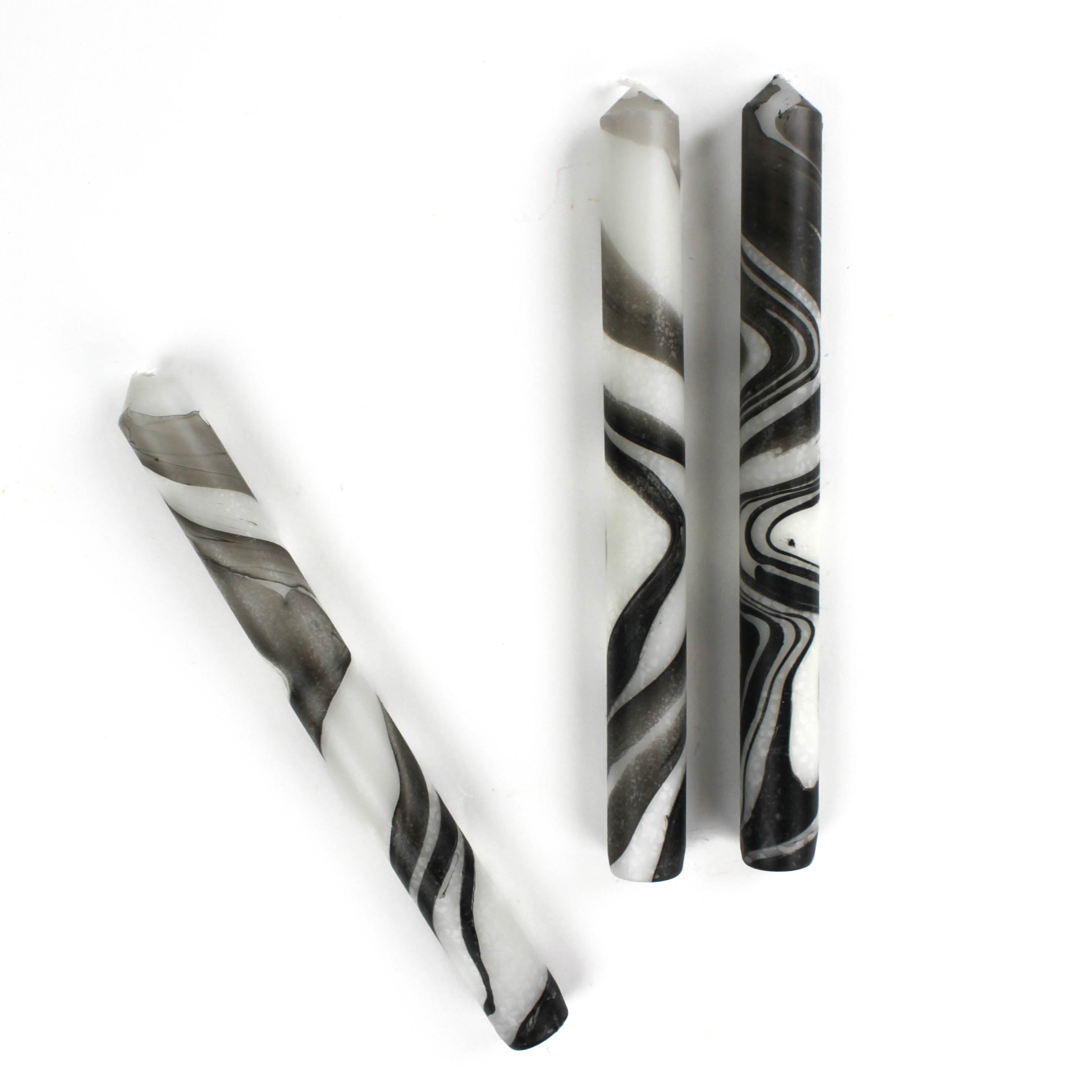 Three marbled black-and-white taper candles are lying horizontally.