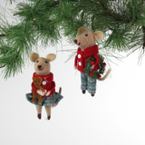 Two felt mouse ornaments wear festive red jackets and blue-green clothing—one holding a teddy bear and the other carrying a holiday wreath— and hanging from pine branches.