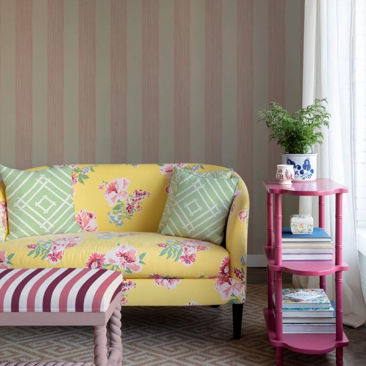 A yellow floral sofa in front of a wall covered in pink striped wallpaper