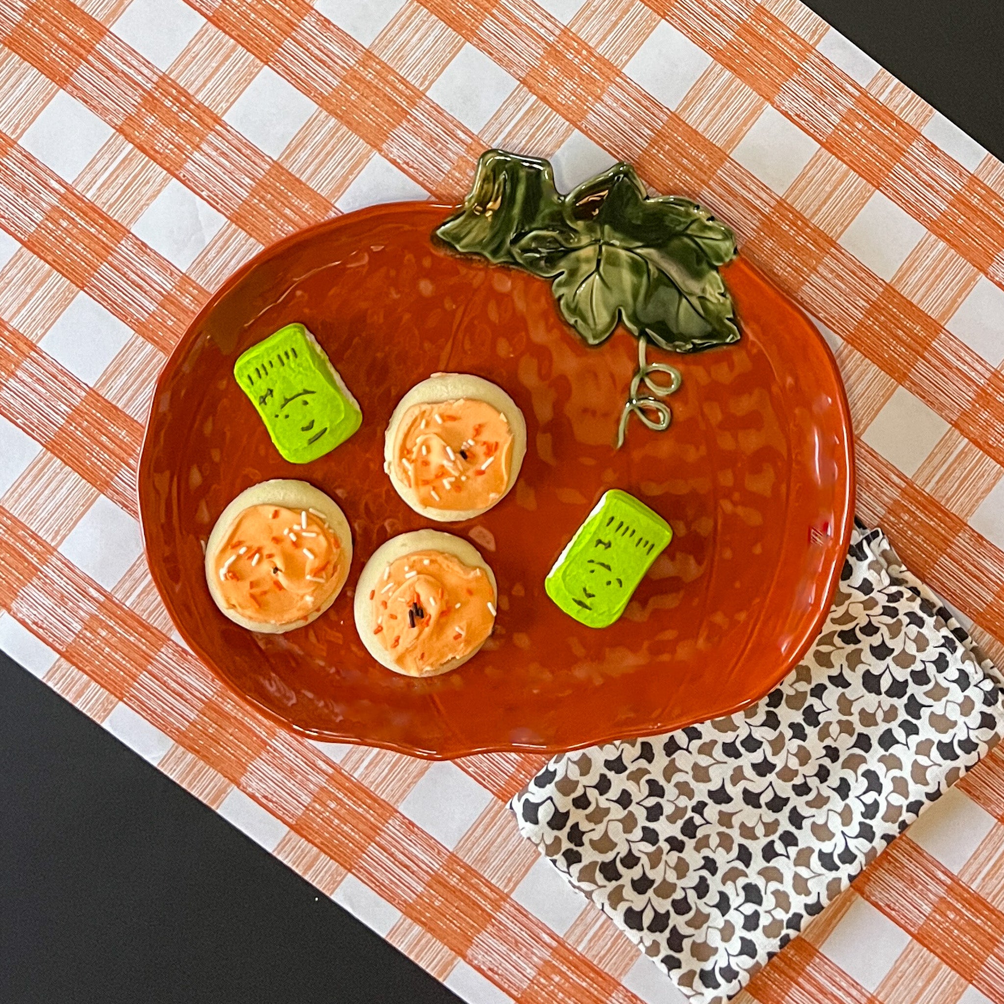 a large orange pumpkin serving platter with 5 halloween cookies on it against an orange paper halloween table runner.