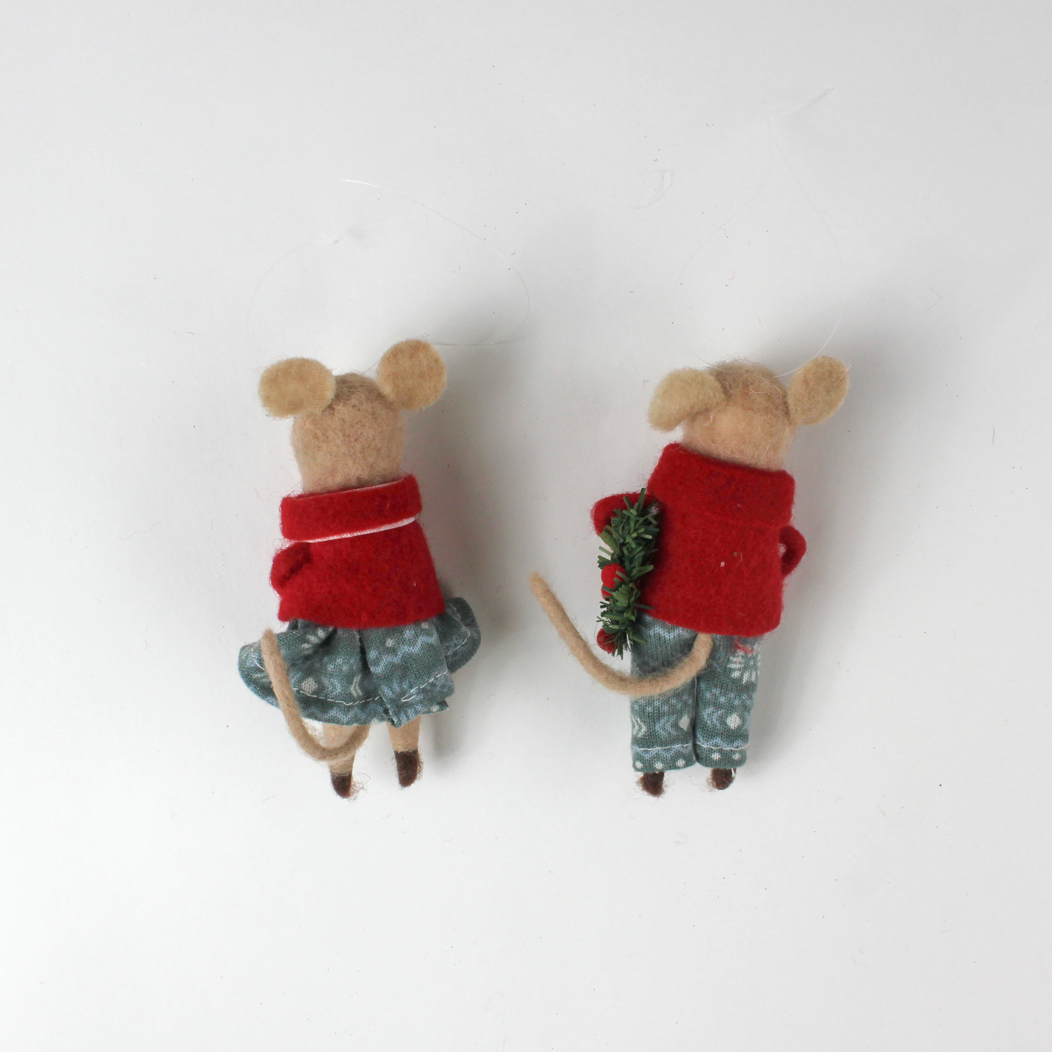 back of Two felt mouse ornaments wear festive red jackets and blue-green clothing—one holding a teddy bear and the other carrying a holiday wreath—lying flat