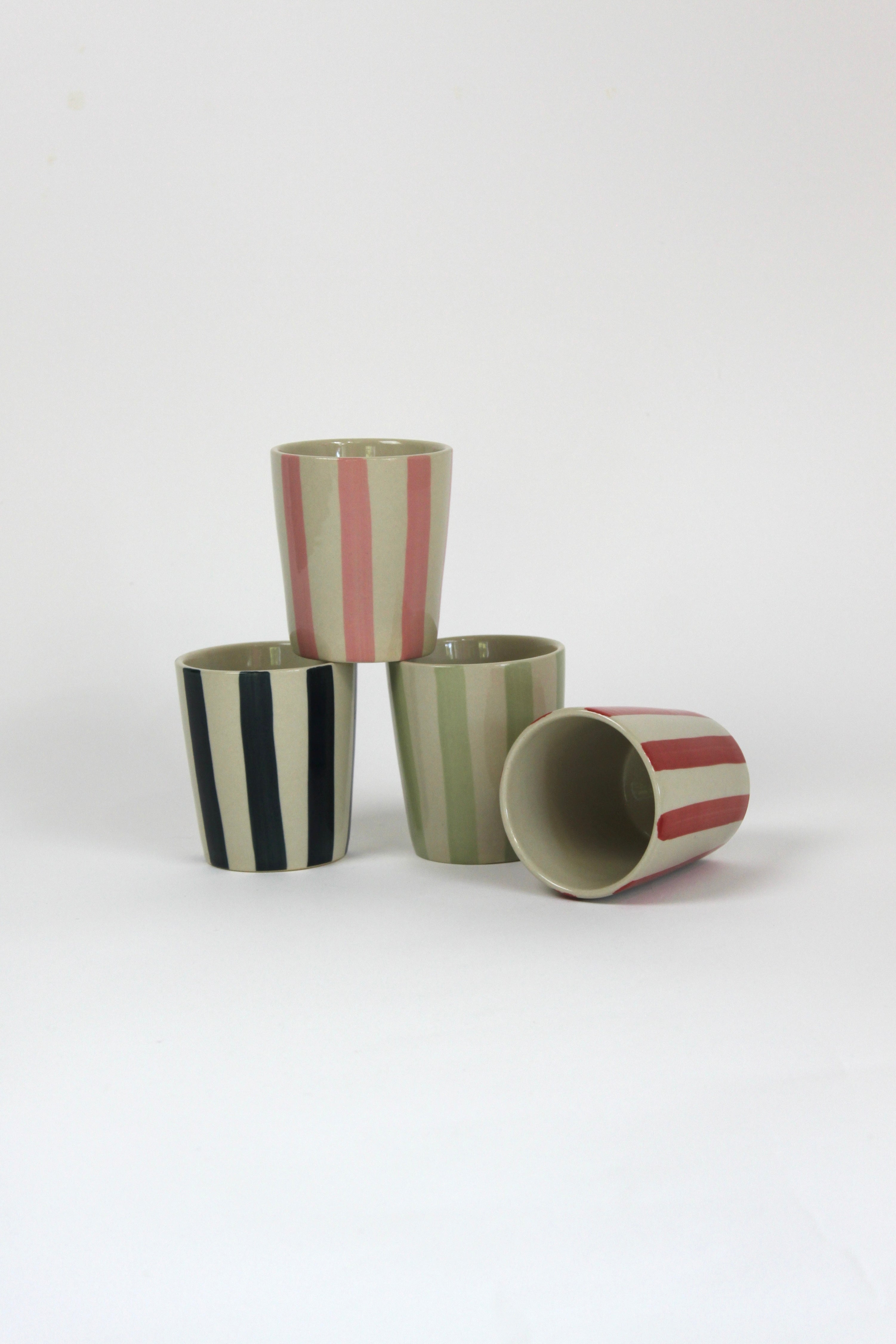 a set of four striped ceramic cups in black, pink, green and red.