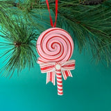 Decorative candy cane ornament with a red and white striped design hanging on a green pine branch.
