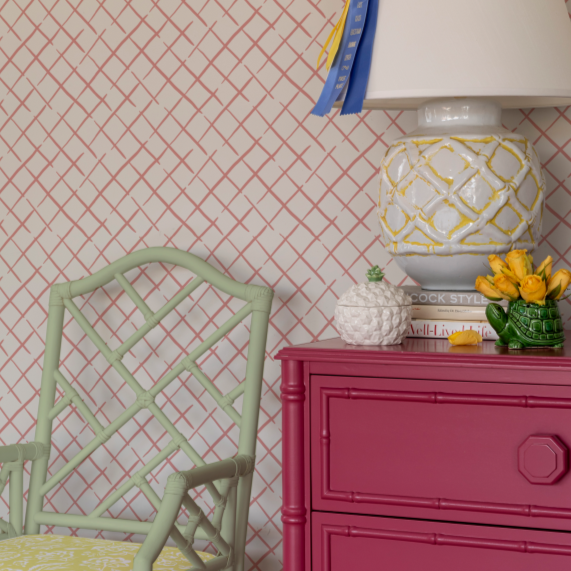 A section of wallpaper with a white lattice pattern, shown in a room with a pink dresser and a green chair.