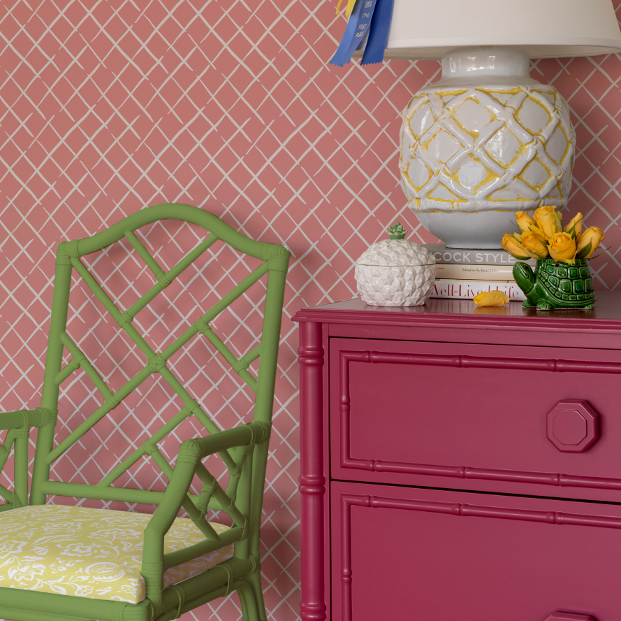 Pink trellis wallpaper with a green bamboo chair and pink chest in front of it