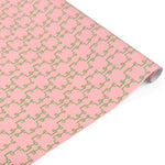 Rolled elegant gift wrapping paper featuring intricate green bamboo lattice patterns on a soft pink background.