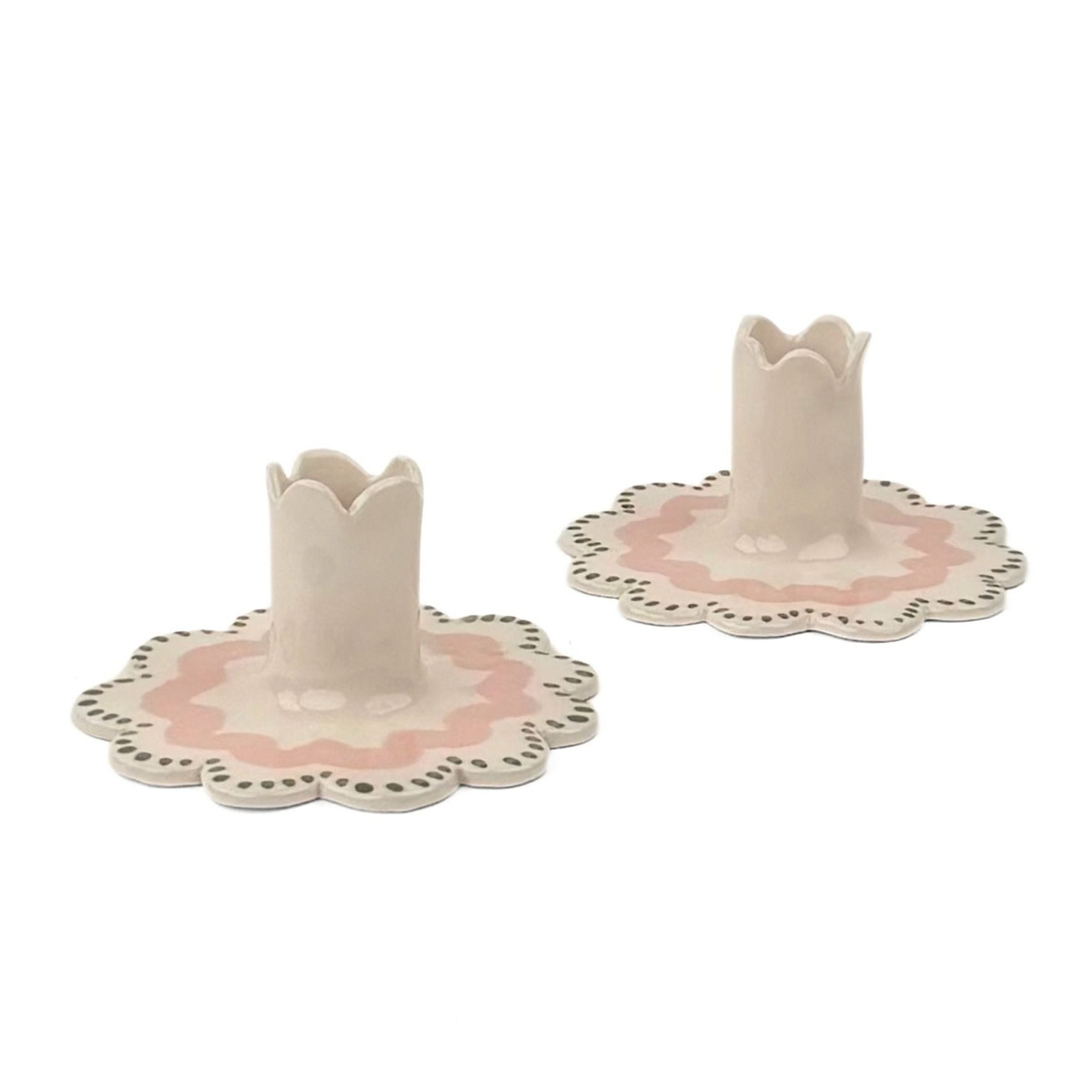 Two matching ceramic candle holders with flower-shaped bases and scalloped edges, decorated in soft pink and cream with small dark dot accents.