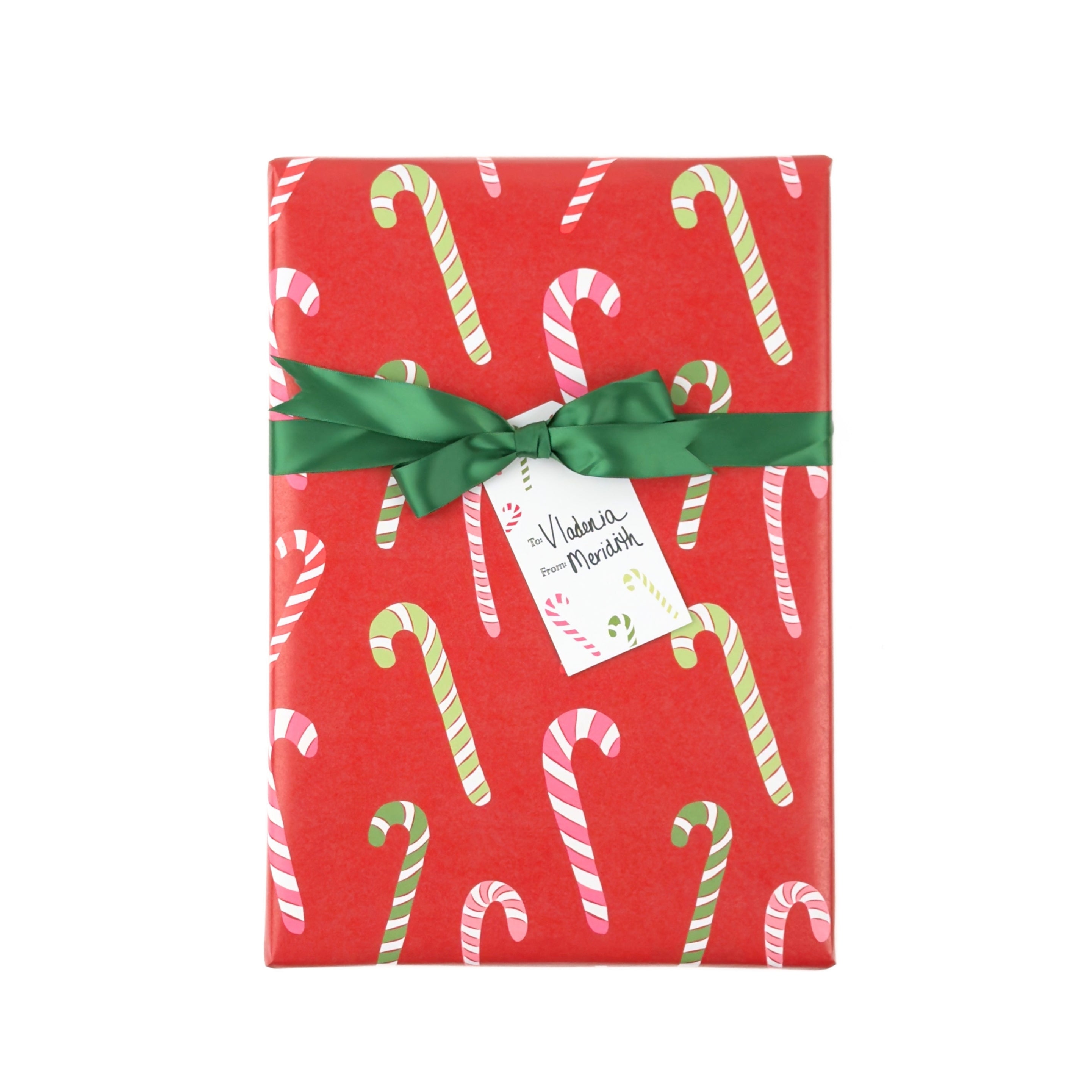A rectangular gift box wrapped in festive red paper with a candy cane pattern, tied with a green ribbon and a small white gift tag.