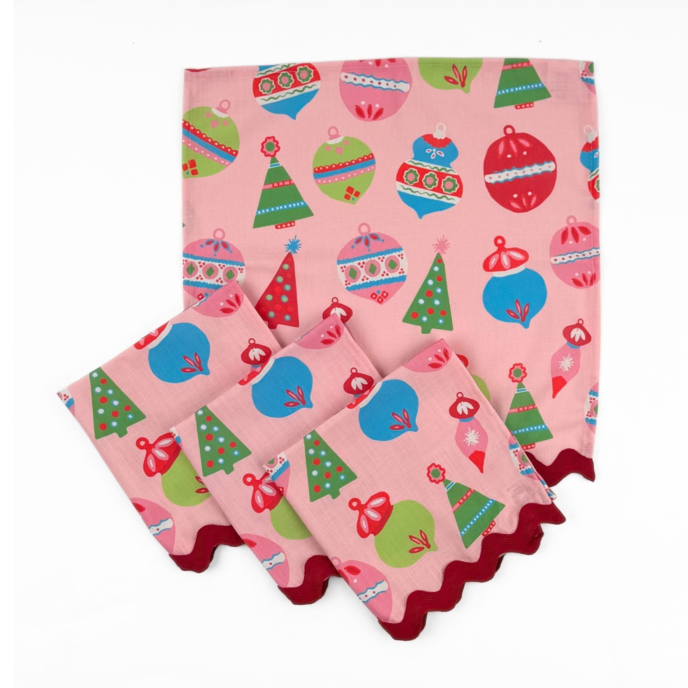Set of Pink Christmas dinner napkins featuring colorful ornaments, festive trees, and red scalloped trim for tablescapes.