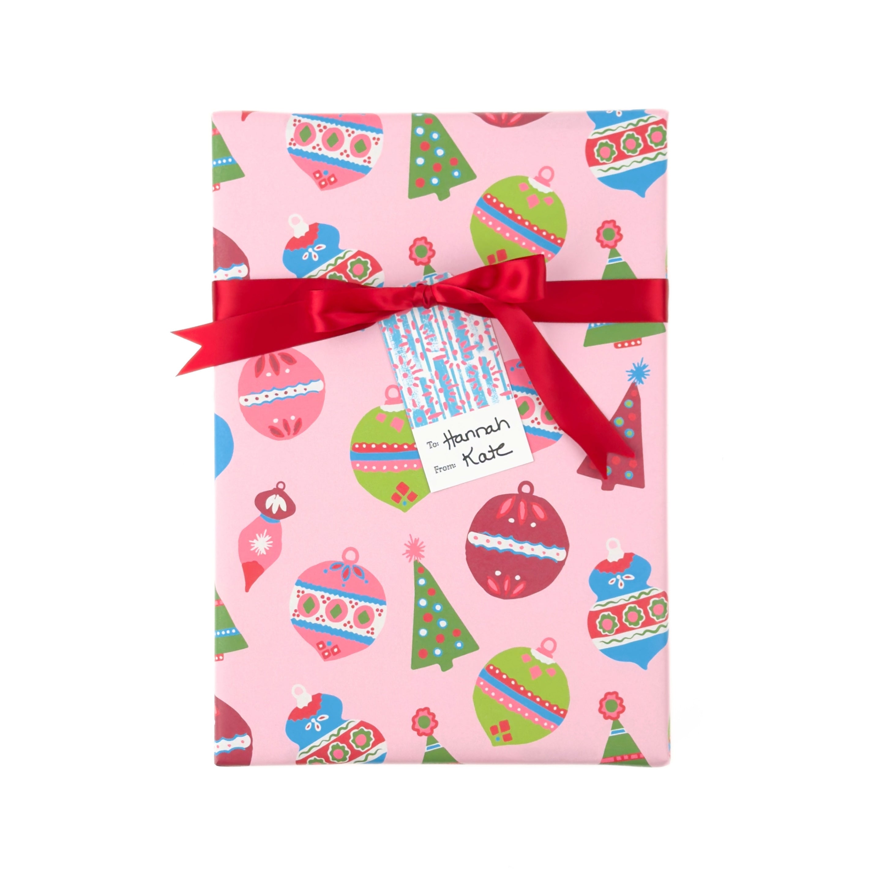 A gift box wrapped in pink Christmas-wrapping paper with a red ribbon and bow, featuring a personalized name tag that reads 'Hannah Kate'.