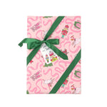 Pink christmas wrapping paper with a whimsical pattern of ballerinas, nutcrackers, and pink wavy lines, tied with a green ribbon and bow on a white background.