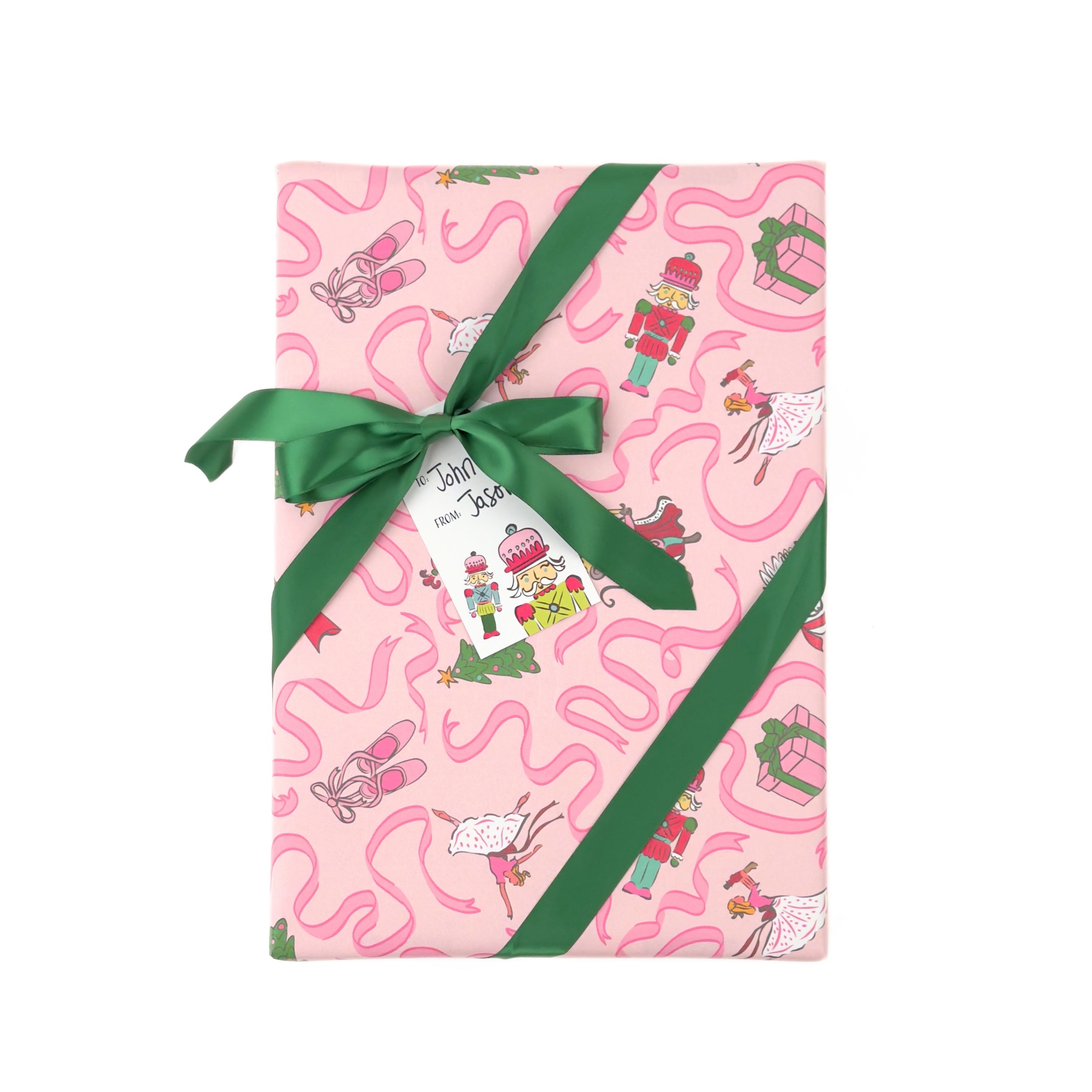 Pink christmas wrapping paper with a whimsical pattern of ballerinas, nutcrackers, and pink wavy lines, tied with a green ribbon and bow on a white background.