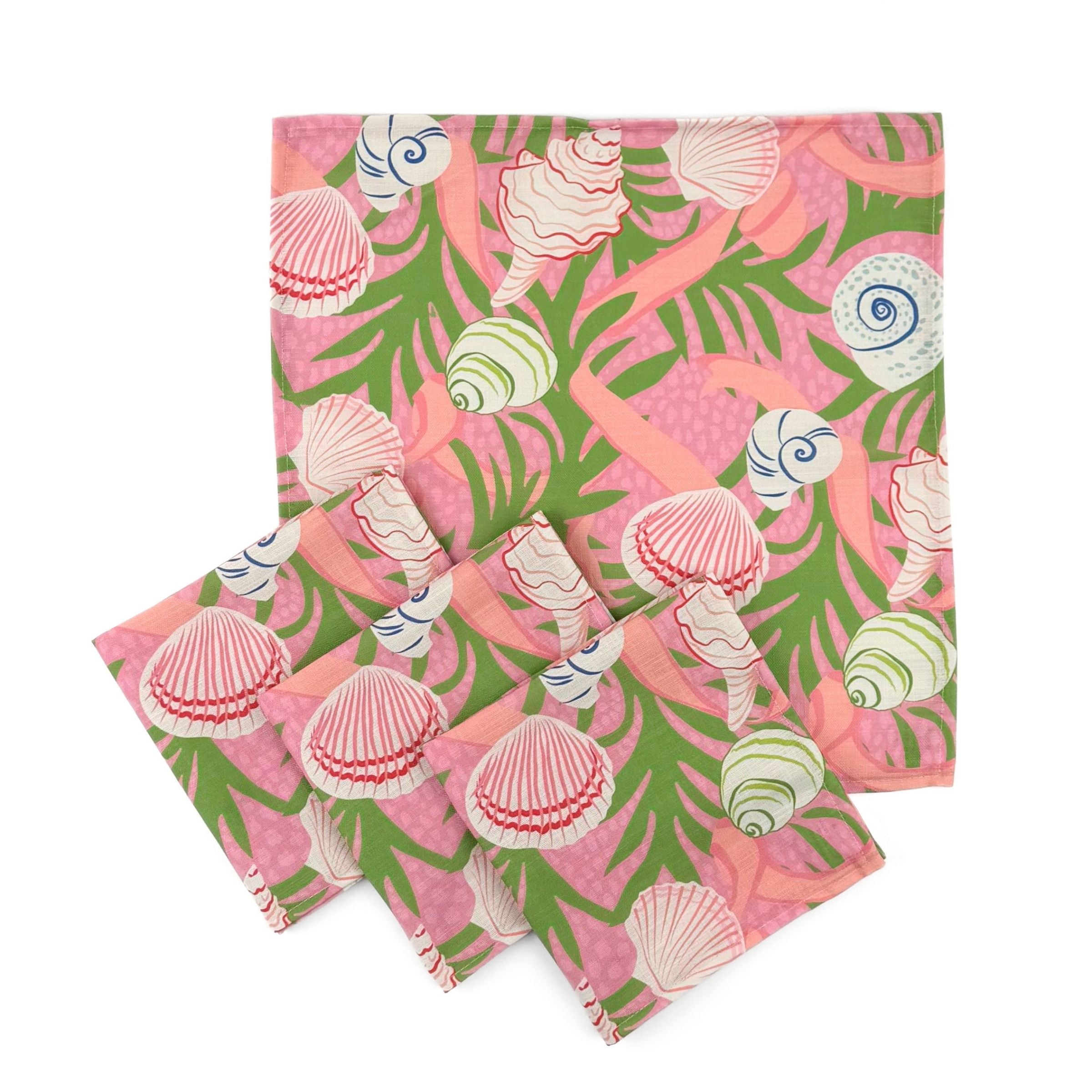 Set of Pink cloth dinner napkins featuring colorful seashells, tropical green foliage, and playful coastal inspired patterns.
