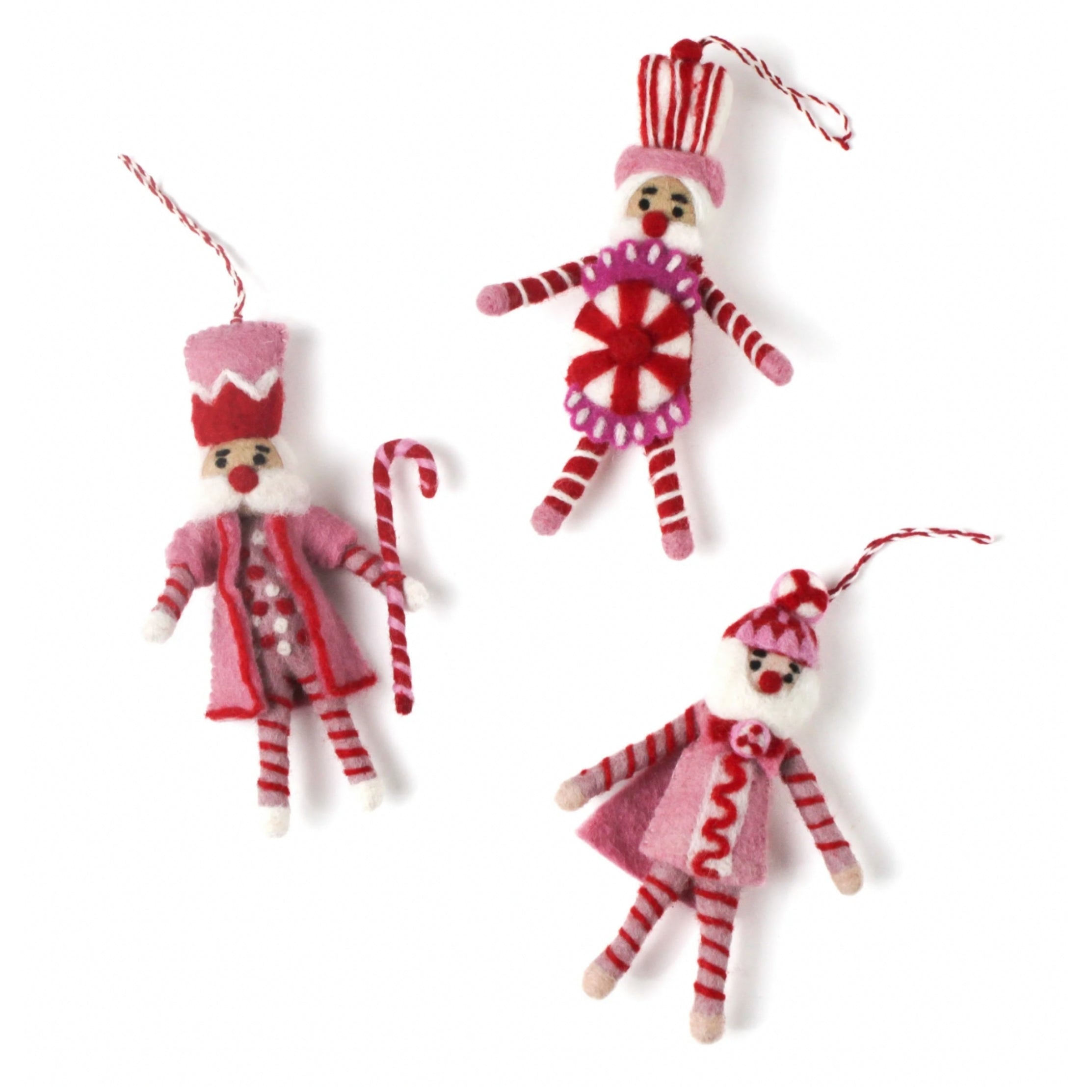 Three Christmas felt nutcracker ornaments in red, pink and white striped outfits on a white background