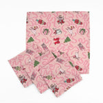 Set of Pink Christmas dinner napkins featuring swirling ribbons, nutcrackers, ballerinas, festive gifts, and whimsical holiday illustrations.