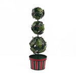 A tole metal three tiered holly topiary ball centerpiece with a striped red and green pot forming the base. 