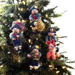 Four felt colonial soldier patriotic Christmas ornaments hanging on a lit Christmas tree. The ornaments feature different soldier designs: one with a flag, one with a drum, one on horseback, and one with a rifle.