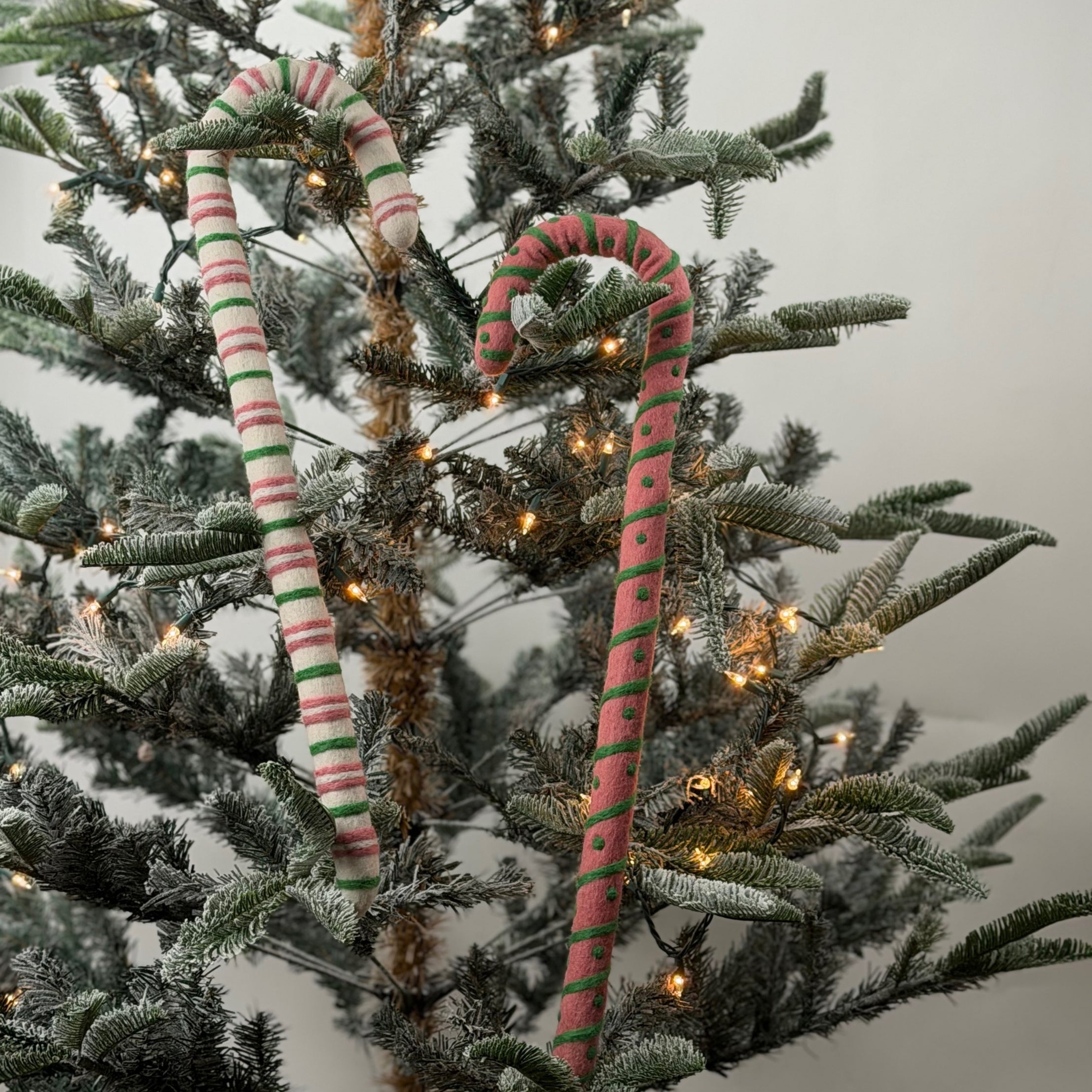 Large felt Christmas candy canes featuring festive pink, green, and cream stripes with playful patterns.