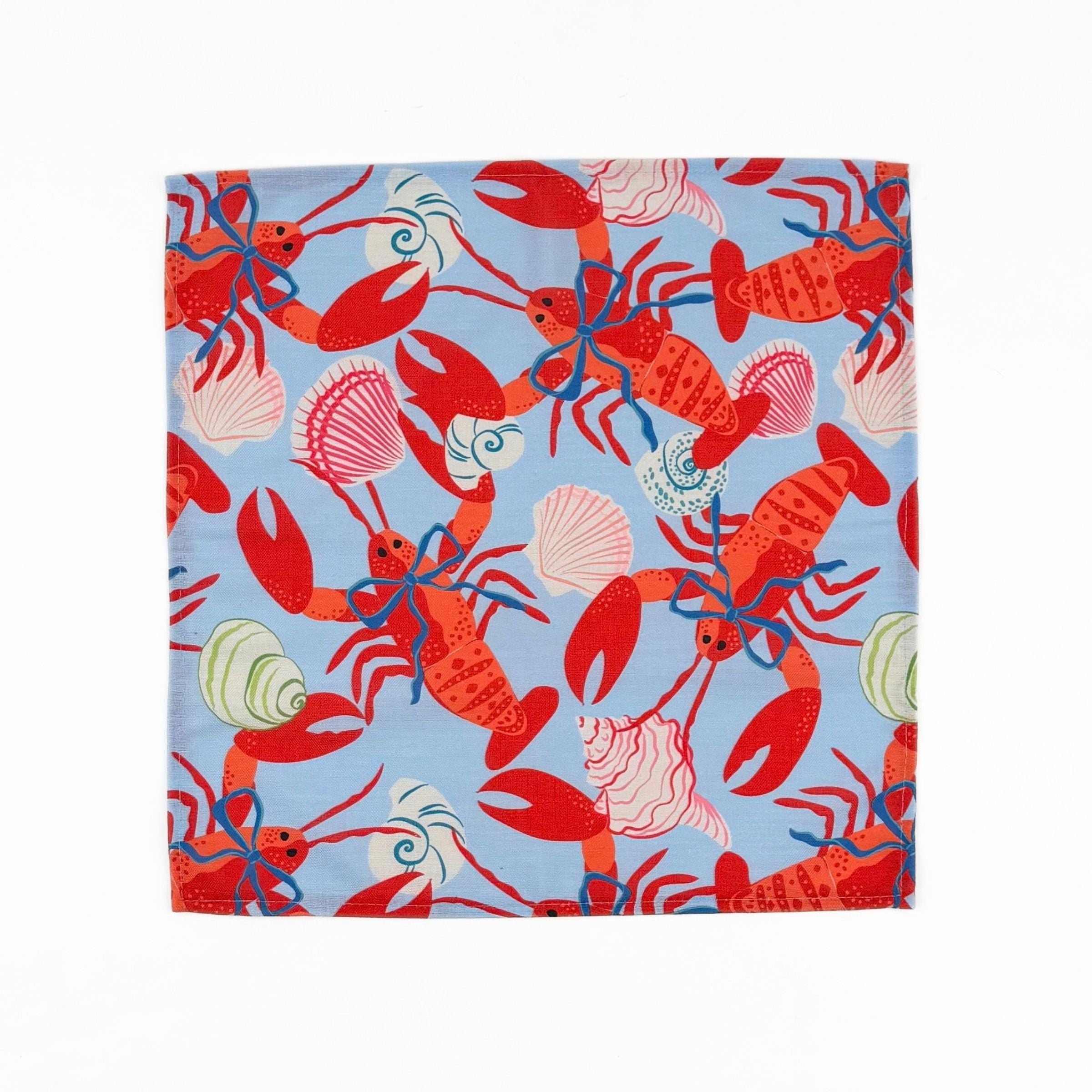 Blue cloth dinner napkins featuring vibrant red lobsters, seashells, and playful coastal patterns for entertaining.