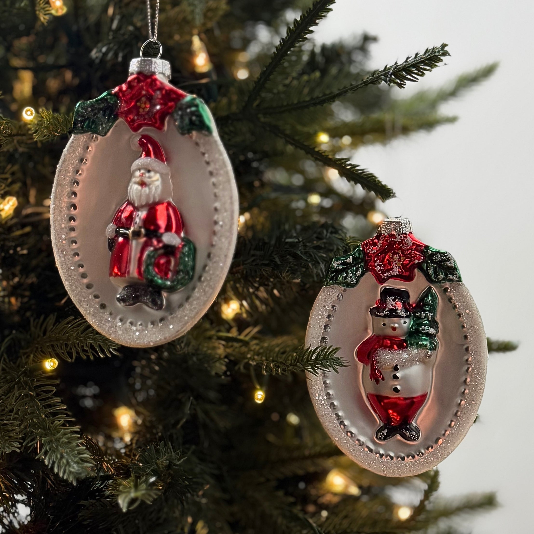 Festive glass Christmas ornaments featuring Santa and snowman designs with sparkling silver, red, and green accents.