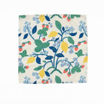 White cloth dinner napkins featuring vibrant strawberries, yellow lemons, blue flowers, and lush green foliage.
