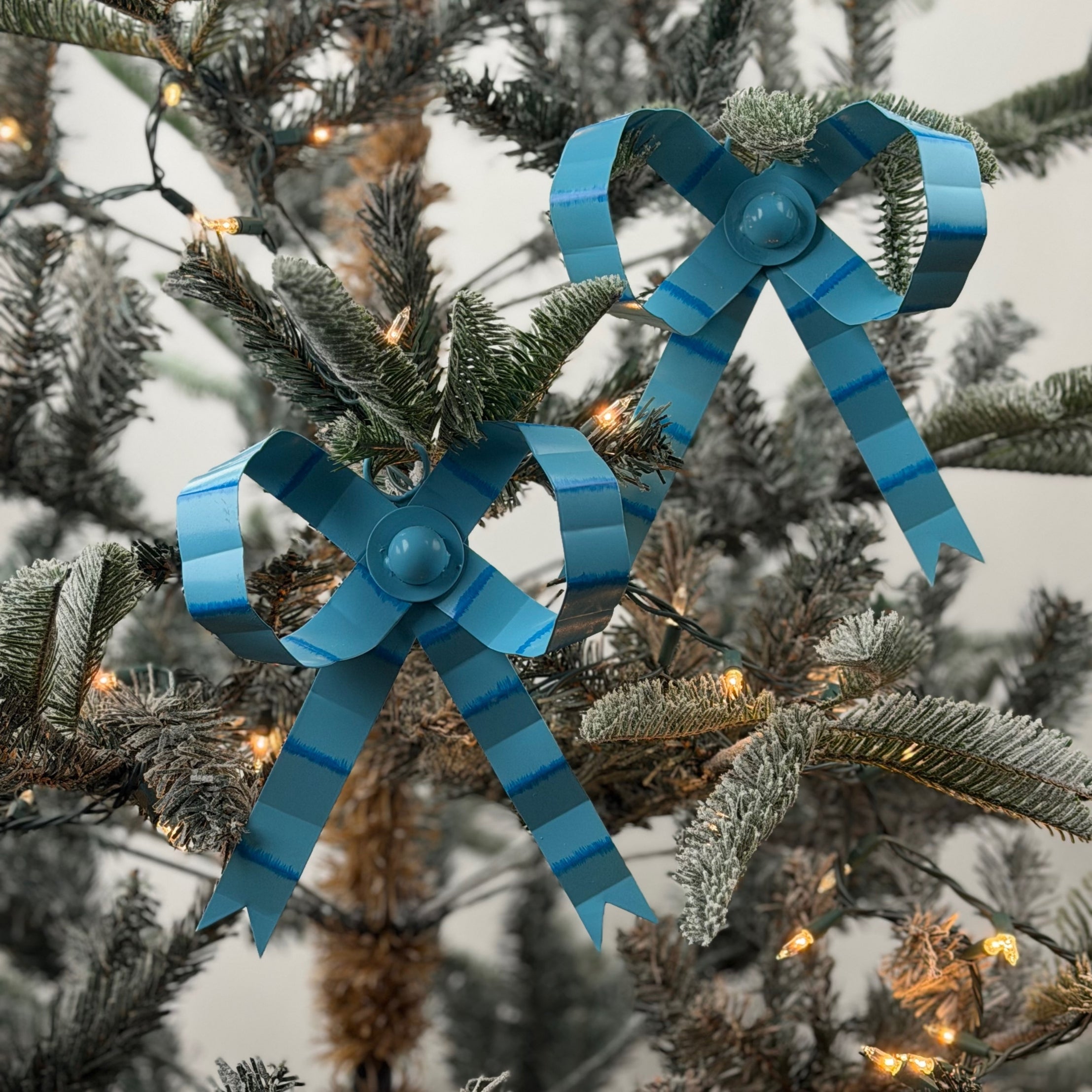 Blue tole Christmas bow ornaments featuring darker blue stripes and charming ribbon loops for festive decorating.
