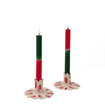 Two lit red taper candles displayed in white ceramic scalloped candle holders with hand-painted red brushstroke accents on a light background.