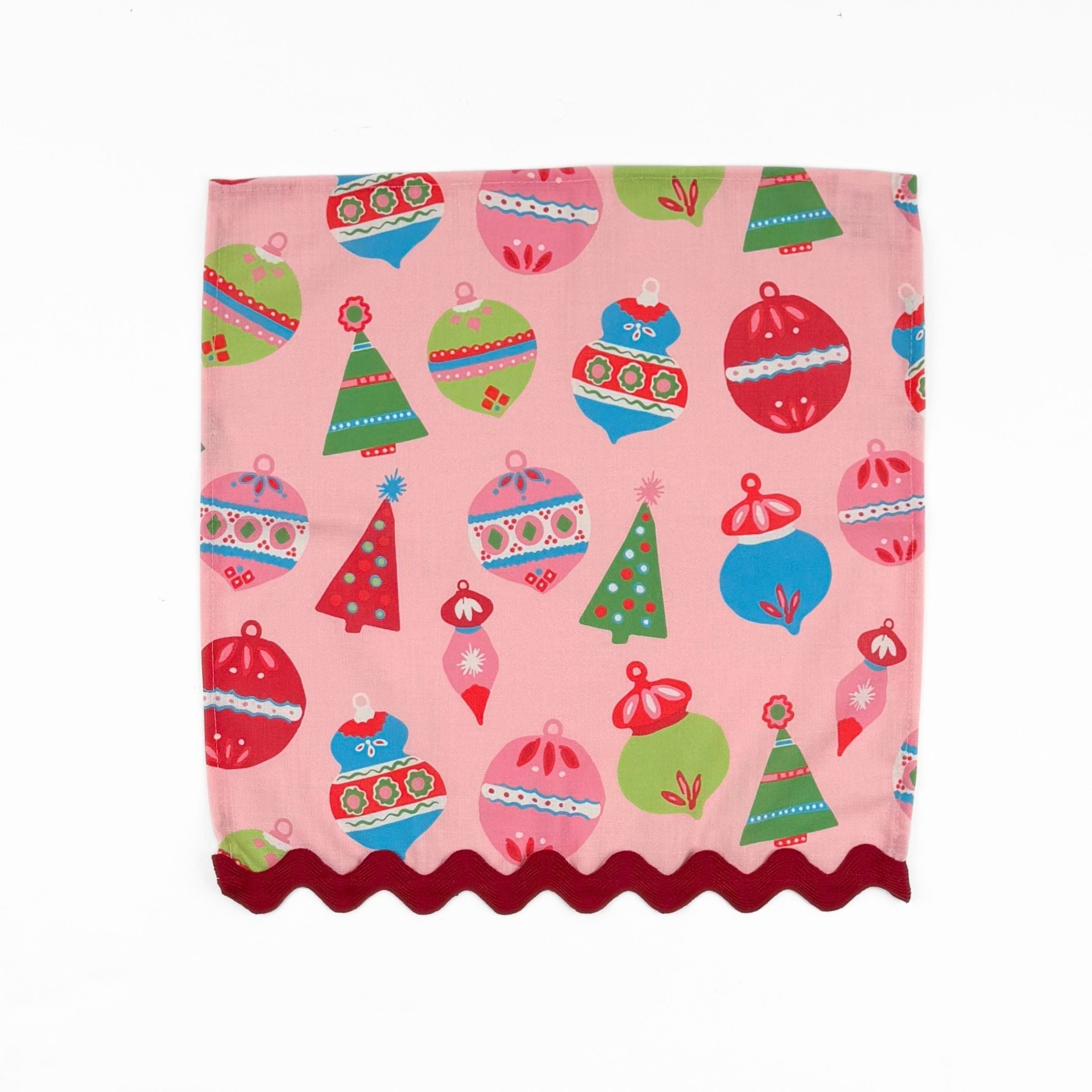 Pink Christmas dinner napkins featuring colorful ornaments, festive trees, and red scalloped trim for tablescapes.