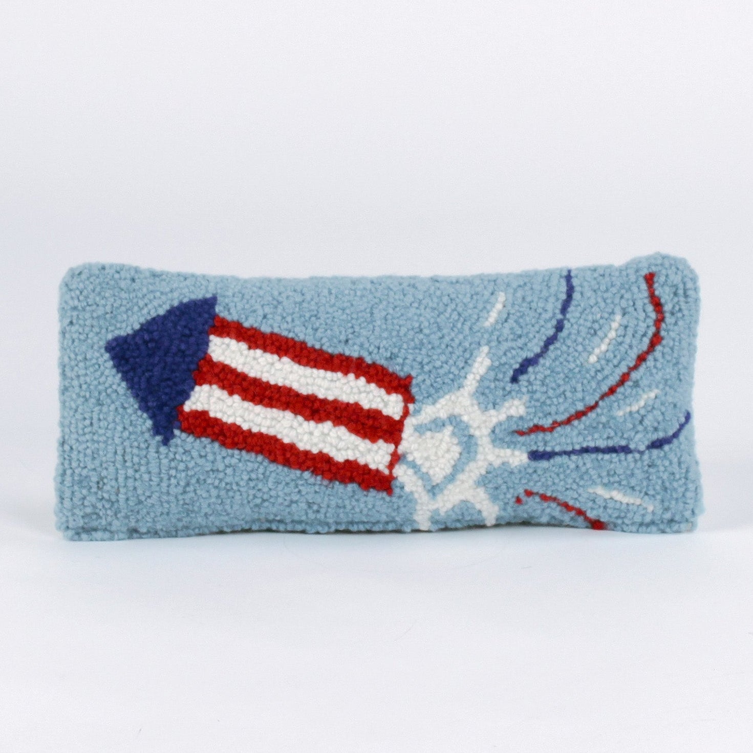 Rectangular blue decorative pillow with a hooked texture featuring a red, white, and blue fireworks rocket design, shown on a white background.
