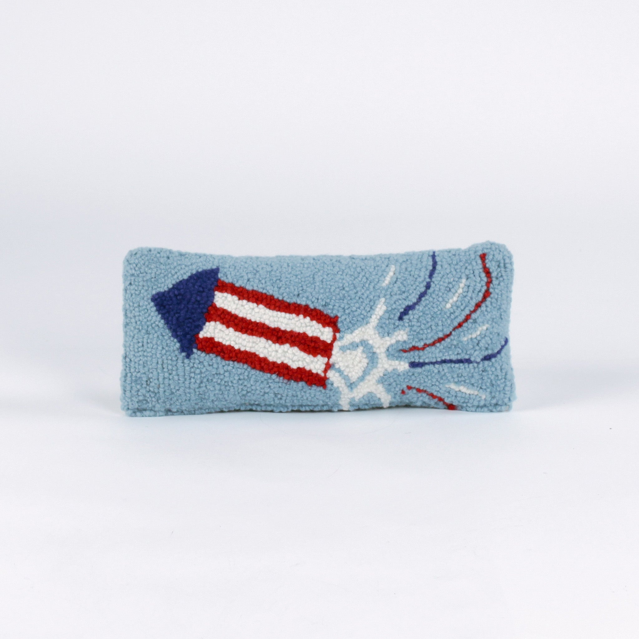 Rectangular blue decorative pillow with a hooked texture featuring a red, white, and blue fireworks rocket design, shown on a white background.