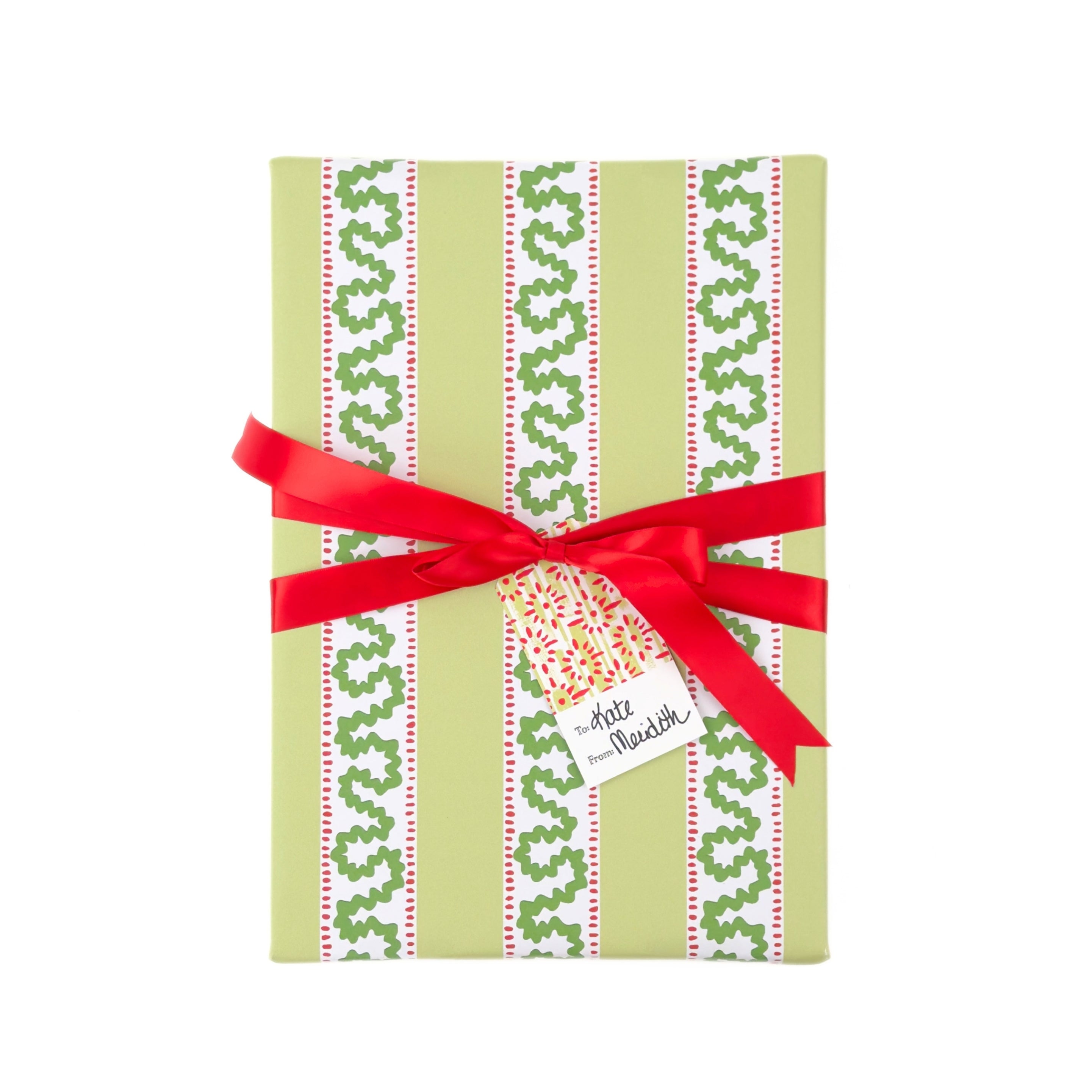 Green patterned Christmas gift box wrapped in holiday paper with decorative green ribbon and tied with red ribbon and a gift tag
