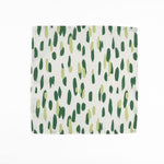 White cloth dinner napkins featuring abstract green brushstroke patterns in varying shades for stylish tablescapes.